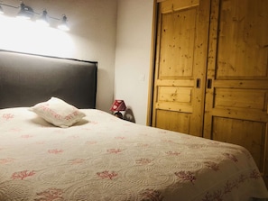 A bedroom with a bed, a wooden wardrobe, a bedside lamp, and a wall-mounted light fixture. - Teppes 46 - Cosy duplex ski in, ski out (LES AVANCHERS VALMOREL)