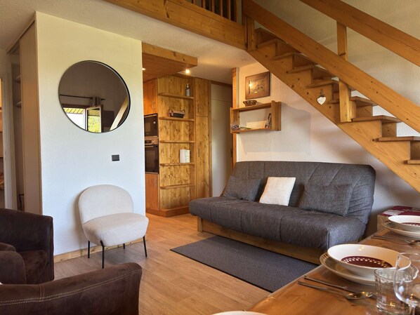 A cozy living room with a grey sofa, a round mirror, wooden shelves, and a staircase. - Teppes 46 - Cosy duplex ski in, ski out (LES AVANCHERS VALMOREL)