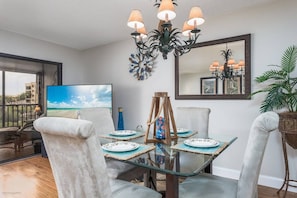 A dining area with a glass table, four chairs, a chandelier, and a large mirror on the wall. - Dock Views, Near Beach, Heated Pool, Private Beach (Sarasota)