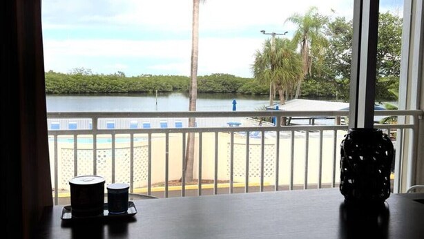 Vista desde una ventana hacia una playa con palmeras y una valla.