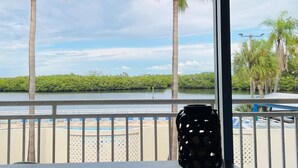 Un balcón con vistas a una playa, palmeras y una extensión de agua.
