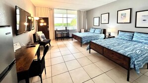 Habitación de hotel con cama, escritorio, silla, televisor y ventana con cortinas.