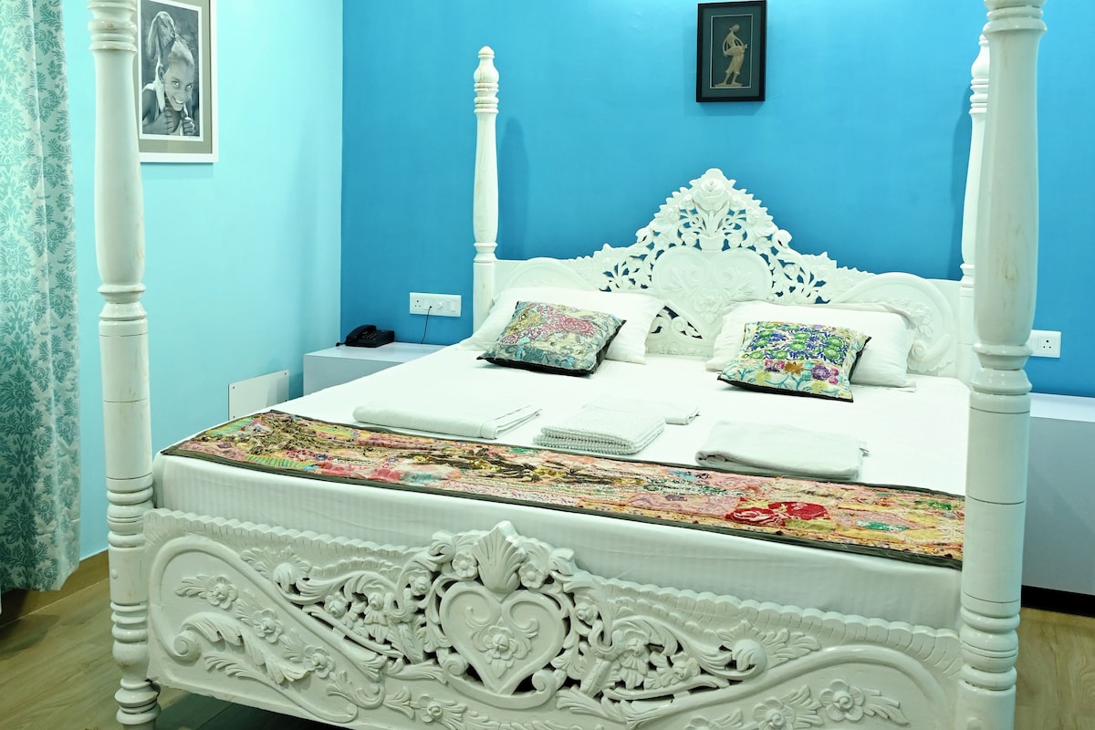 A bedroom with a white four-poster bed, blue walls, and a ceiling fan.