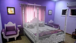 Ein Schlafzimmer mit Himmelbett, einem violetten Sessel und einem kleinen Tisch.