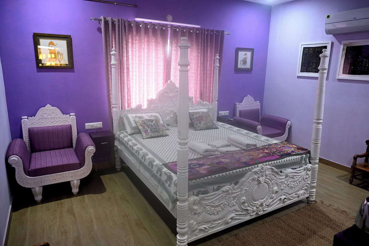 A bedroom with a four-poster bed, a purple armchair, and a small table.