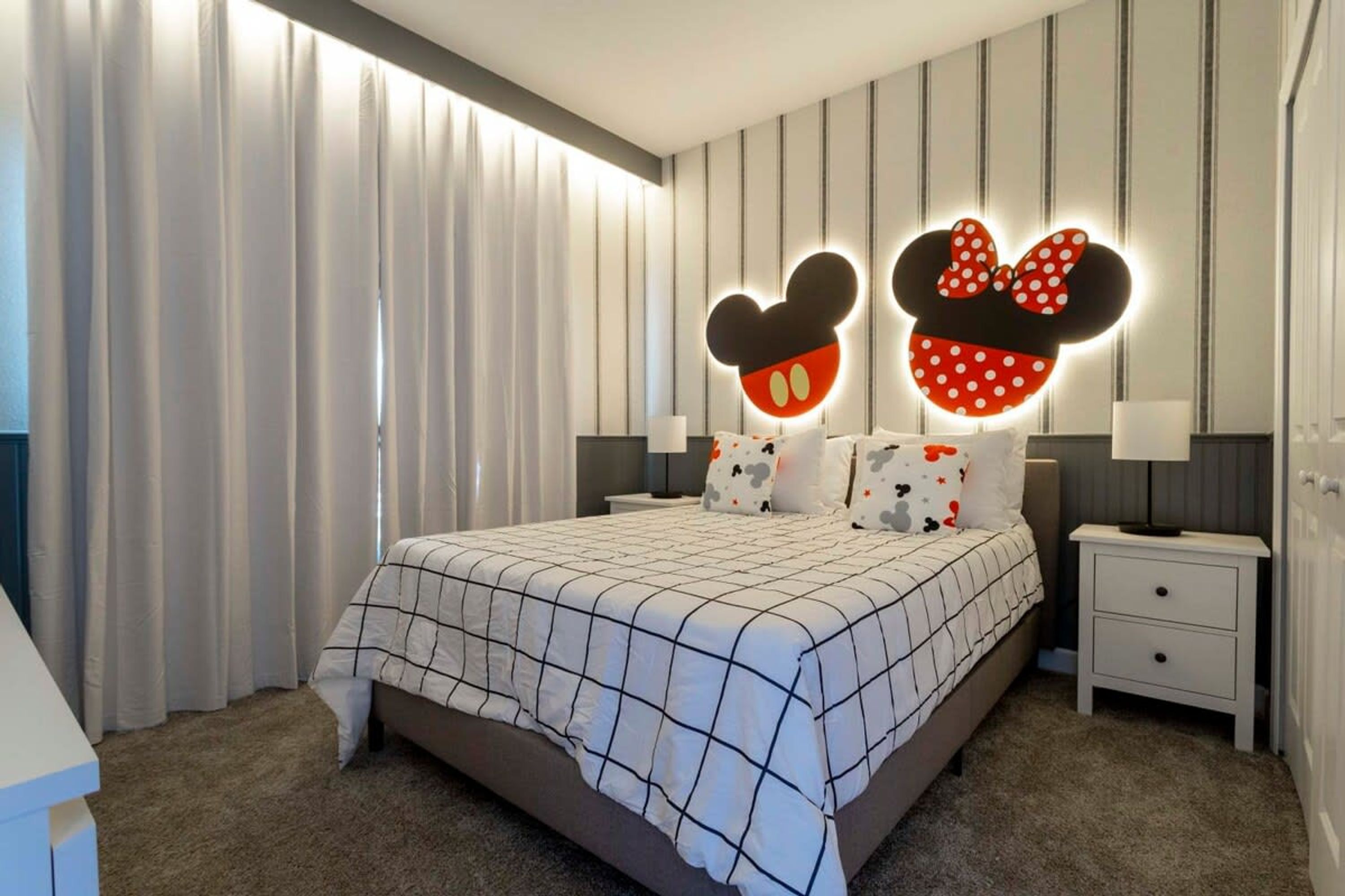 A modern bedroom with a large bed, Mickey Mouse head-shaped wall lights, striped wallpaper, and a small bedside table.