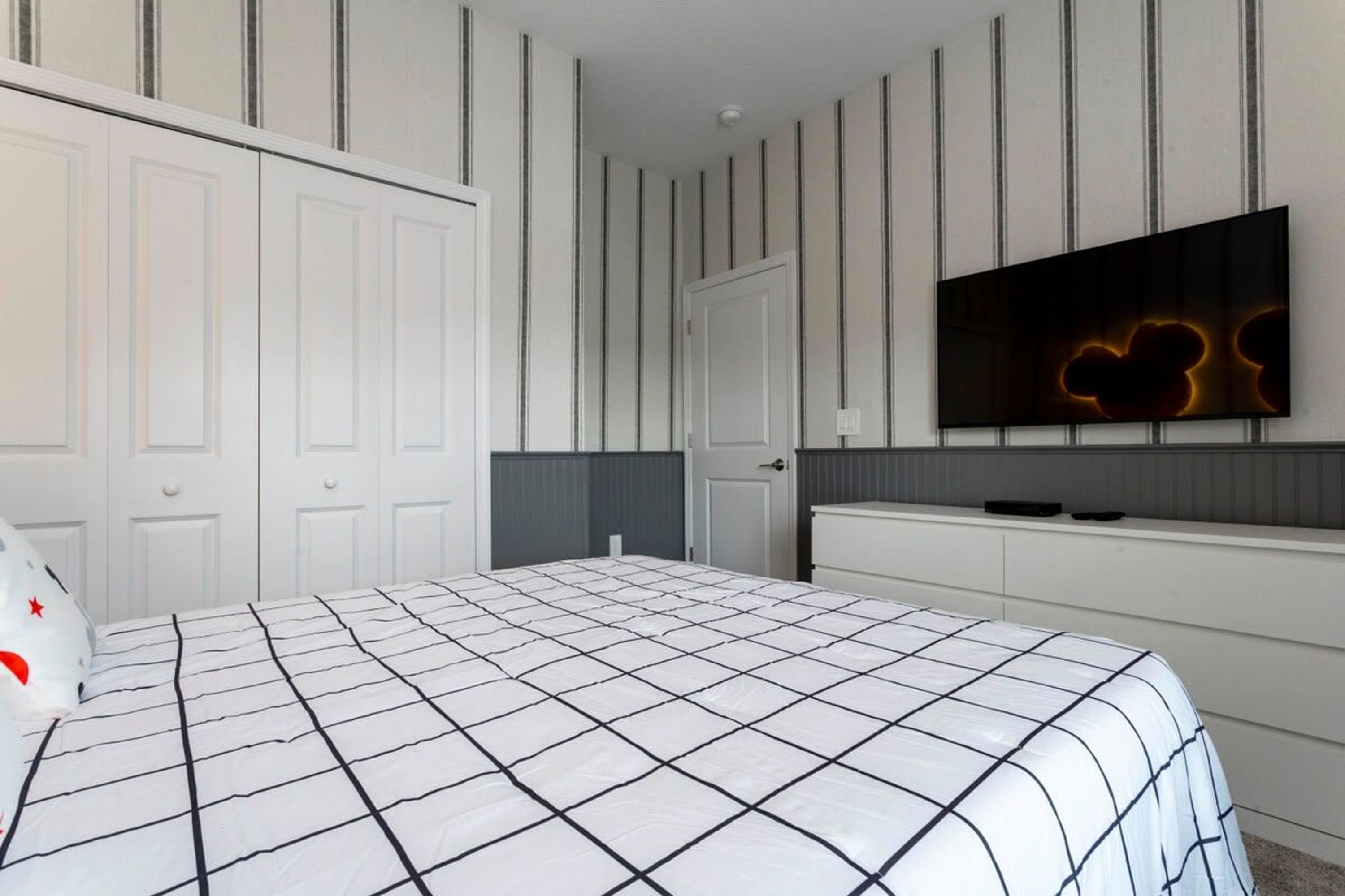 Ein Schlafzimmer mit einem Bett, einem an der Wand montierten Fernseher und einem Kleiderschrank.