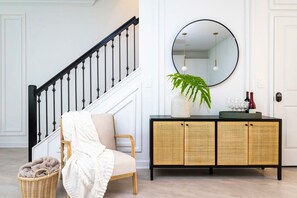 Uma escadaria com balaústres pretos, uma cadeira de vime com um cobertor branco e um console de vime com um espelho e uma planta.
