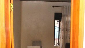 Una habitación con suelo de baldosas, una silla, un ventanal con cortinas y un marco de puerta.