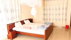 Un dormitorio con una cama de madera, una mesita de noche, un cubo rojo y cortinas estampadas.