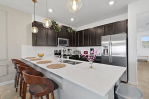 A modern kitchen with dark cabinets, a white island, stainless steel appliances, and pendant lighting. - Magical Getaway - Super Cute 3BR Apartment (Davenport)