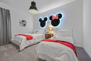 A hotel room with two beds, a Mickey Mouse head wall decoration, a ceiling light, and a small bedside table with a lamp. - Magical Getaway - Super Cute 3BR Apartment (Davenport)