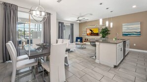 Une cuisine moderne dotée d’un îlot central, d’un coin repas avec des chaises blanches et d’un espace de vie comprenant un canapé et un téléviseur.