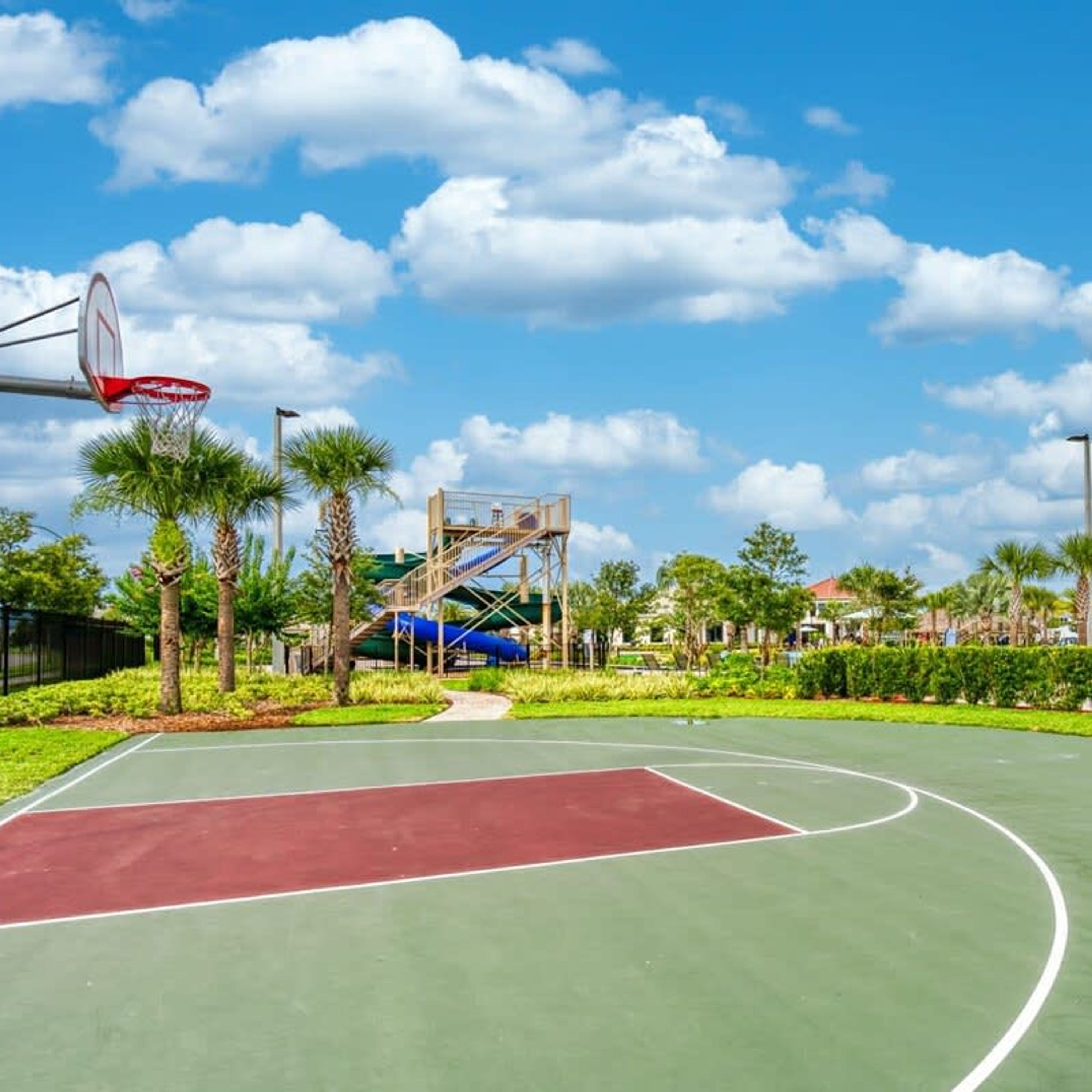 Un terrain de basket en plein air, avec un ciel dégagé et des palmiers.