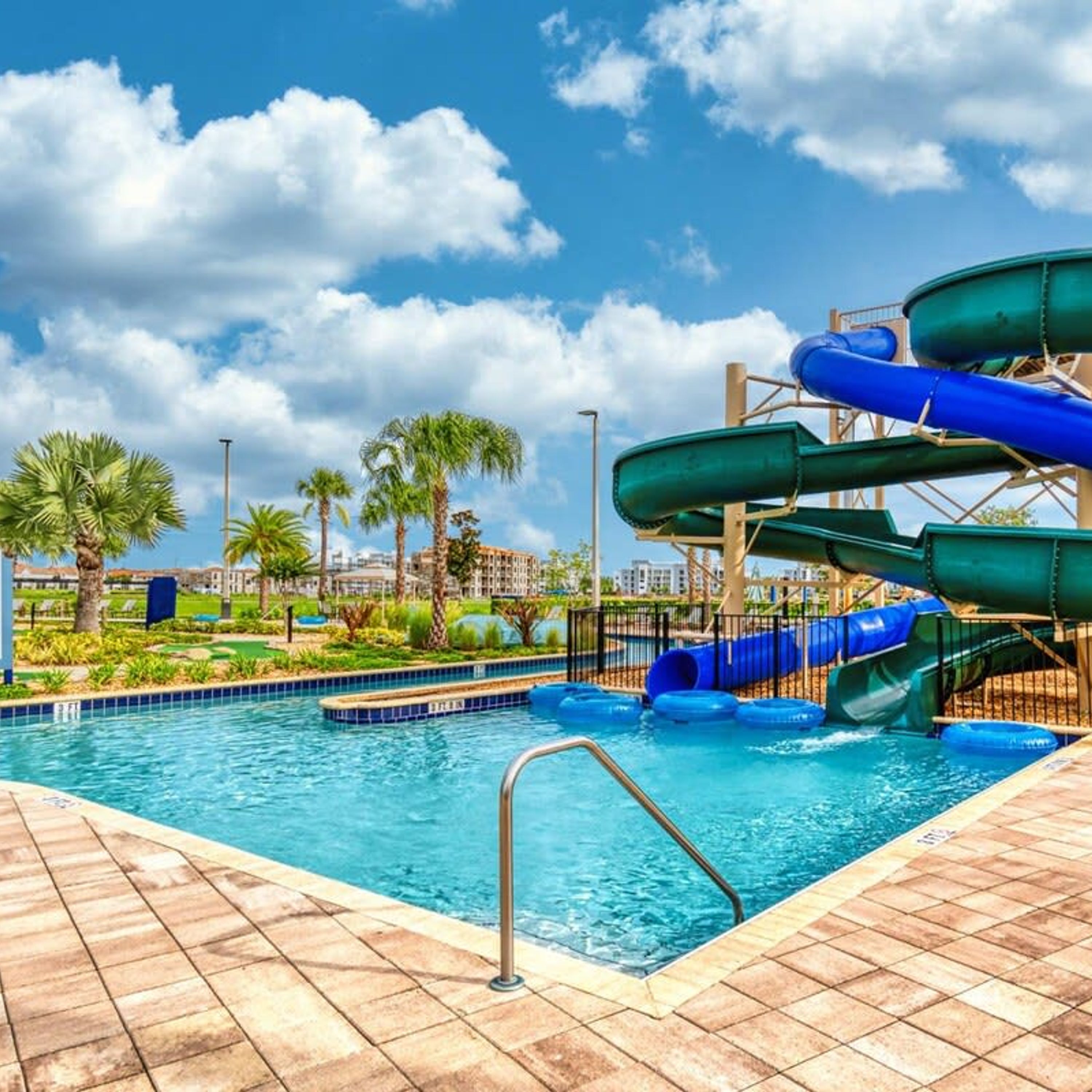 A swimming pool with a water slide, palm trees, and a clear sky.
