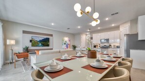 Un espace repas moderne avec une longue table dressée pour six personnes, entourée de chaises de couleur beige.