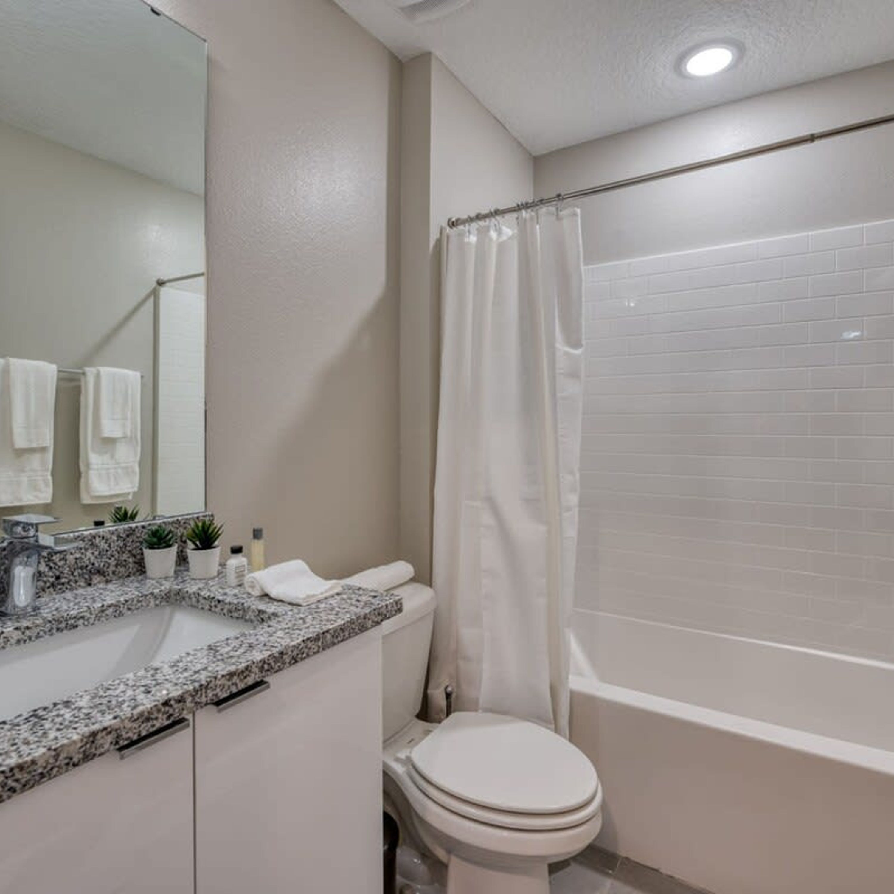 A modern bathroom with a granite countertop sink, a toilet, and a bathtub.