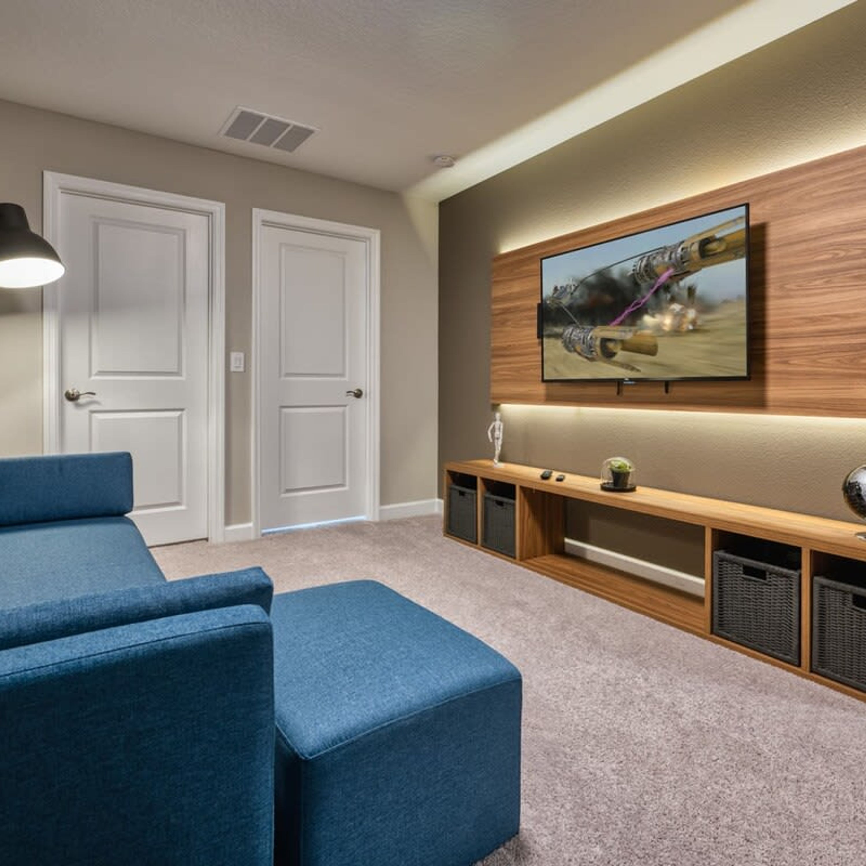 Ein Heimkinozimmer mit einem großen Flachbildfernseher an der Wand, einem blauen Sofa und einer Holz-Unterhaltungsecke mit Stauraum.