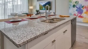 Una cocina moderna con encimeras de granito, un lavamanos de acero inoxidable y un comedor con mesa y sillas.