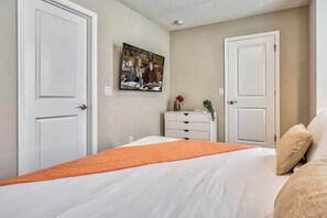 A bedroom with a bed, two white doors, a dresser, and a painting on the wall. - Luxury 5 Bedroom Home 10 Minutes From Disney (Kissimmee)