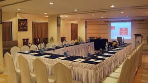 A conference room with a long table, white chairs, and a projector screen. - Hotel Ashok Palace (Manmangalam)