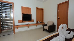 A hotel room with a bed, a TV mounted on the wall, a chair, and a door. - Hotel Ashok Palace (Manmangalam)