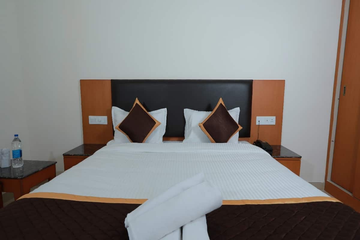 A neatly made bed with a quilted brown bedspread, two white pillows, and two brown pillows with wooden trim. There is a folded towel at the foot of the bed.