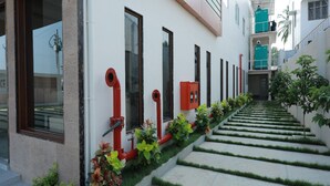 A modern building with a clean facade, a series of windows, and a staircase with green grass edging. - Hotel Ashok Palace (Manmangalam)