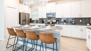 A modern kitchen with white cabinets, a central island with bar stools, stainless steel appliances, and pendant lighting.