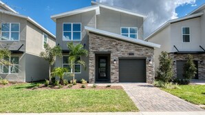 A modern two-story house with a stone facade, a garage, and a well-maintained lawn.