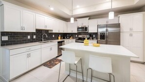 A modern kitchen with white cabinets, a black tiled backsplash, stainless steel appliances, and a central island with bar stools. - 3BR Apartment - Great Location Super Comfort (Kissimmee)