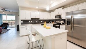 A modern kitchen with white cabinets, a stainless steel refrigerator, and a central island with bar stools. - 3BR Apartment - Great Location Super Comfort (Kissimmee)