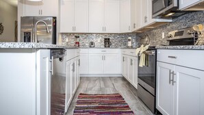 A modern kitchen with white cabinets, stainless steel appliances, a granite countertop, and a colorful woven rug.