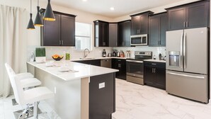 A modern kitchen with dark cabinets, stainless steel appliances, a white island with bar stools, and pendant lighting.