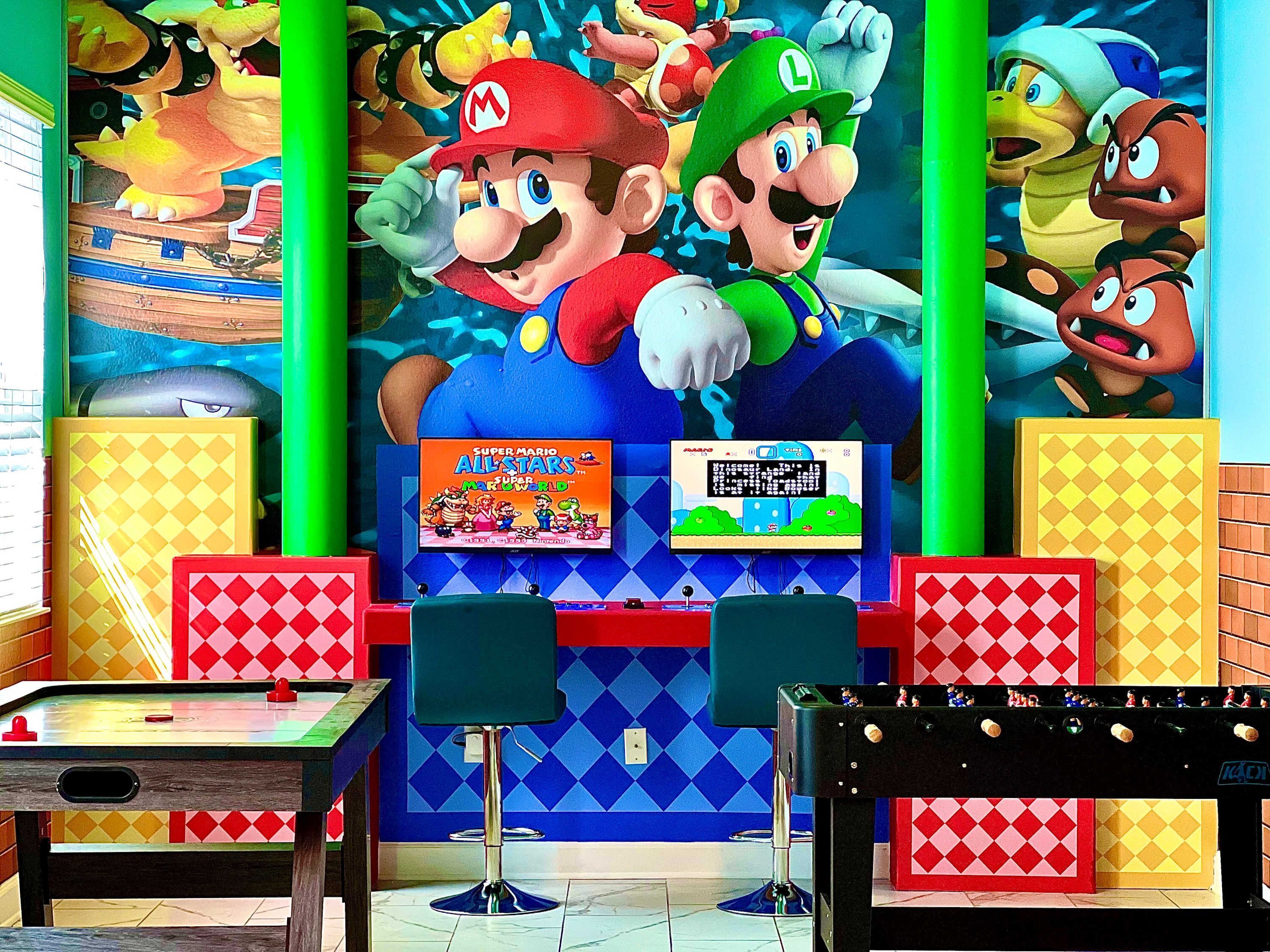 Une pièce décorée d’une fresque murale sur le thème de Mario, avec une table de baby-foot et un téléviseur diffusant « Super Mario All-Stars ».