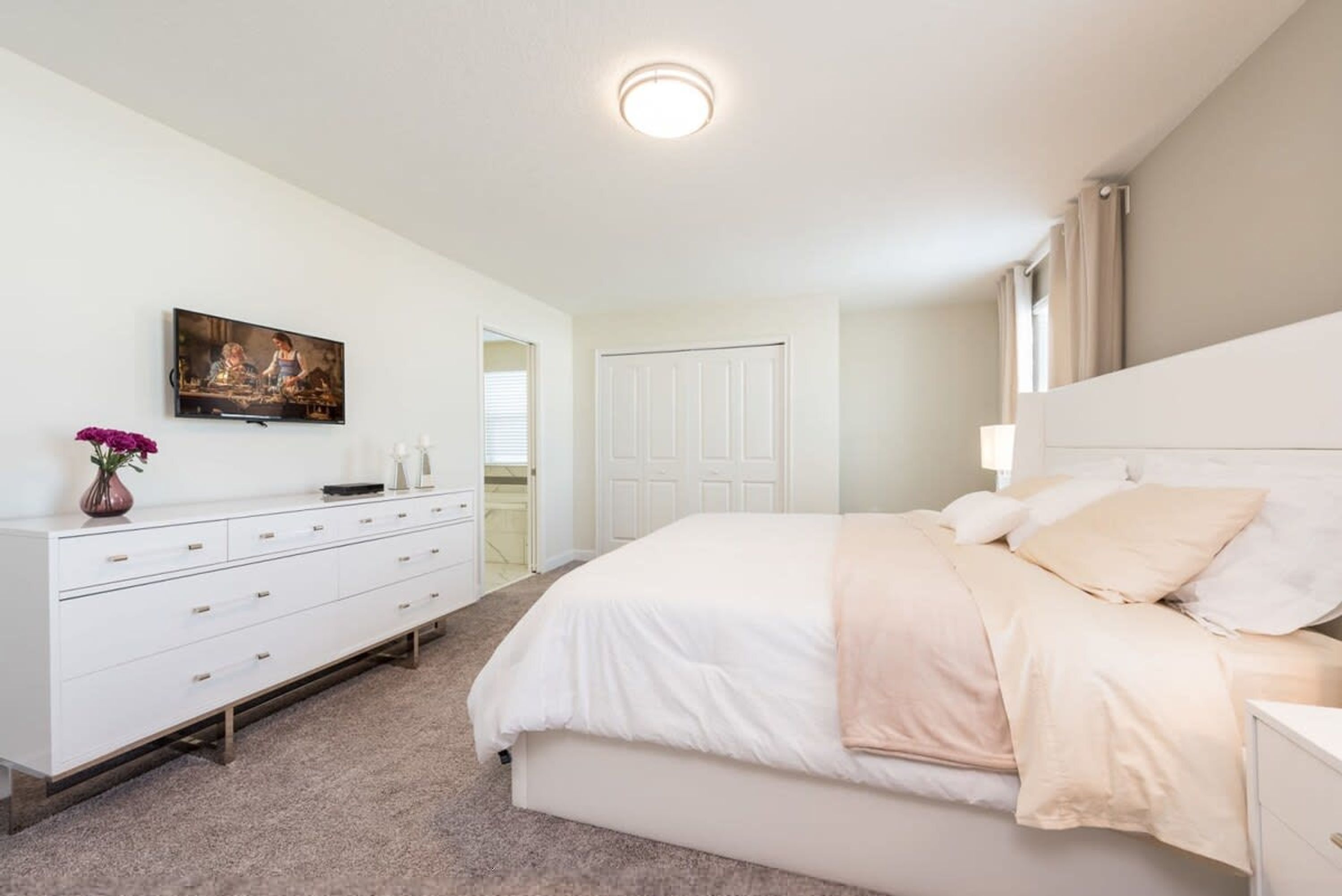 A bedroom with a bed, a dresser, a painting on the wall, and a door leading to another room.
