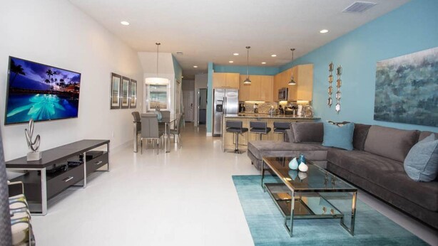A modern living room with a flat-screen TV, a sofa, a coffee table, and a dining area with chairs. - Charming Cozy Haven in Four Corners (Clermont)