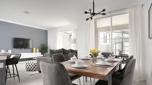 A modern dining area with a wooden table set for four, grey upholstered chairs, and a chandelier above. - Charming Mickey-themed Home Prime Location (Kissimmee)