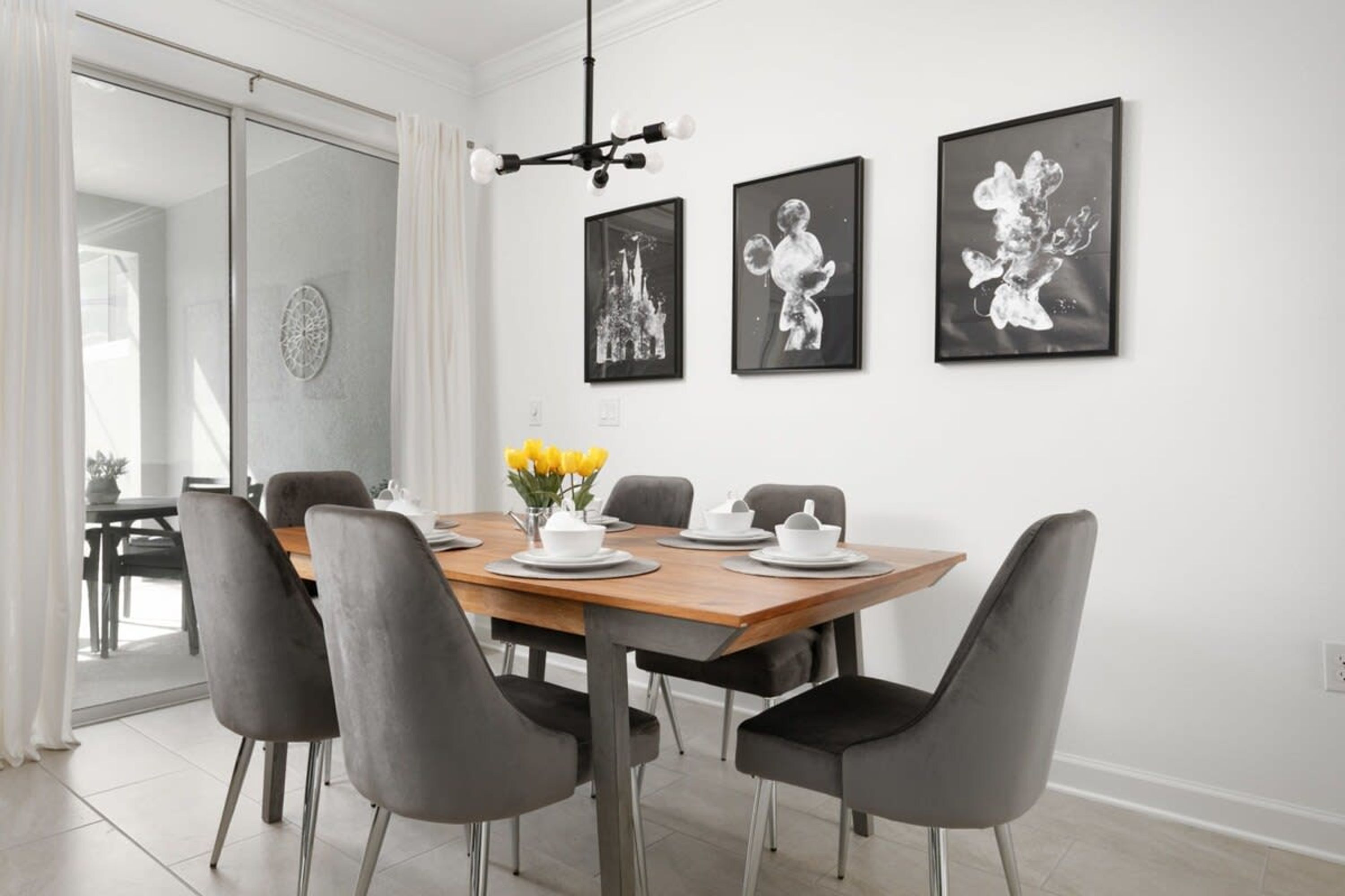 A dining area with a wooden table, grey chairs, and black framed artwork on the wall.