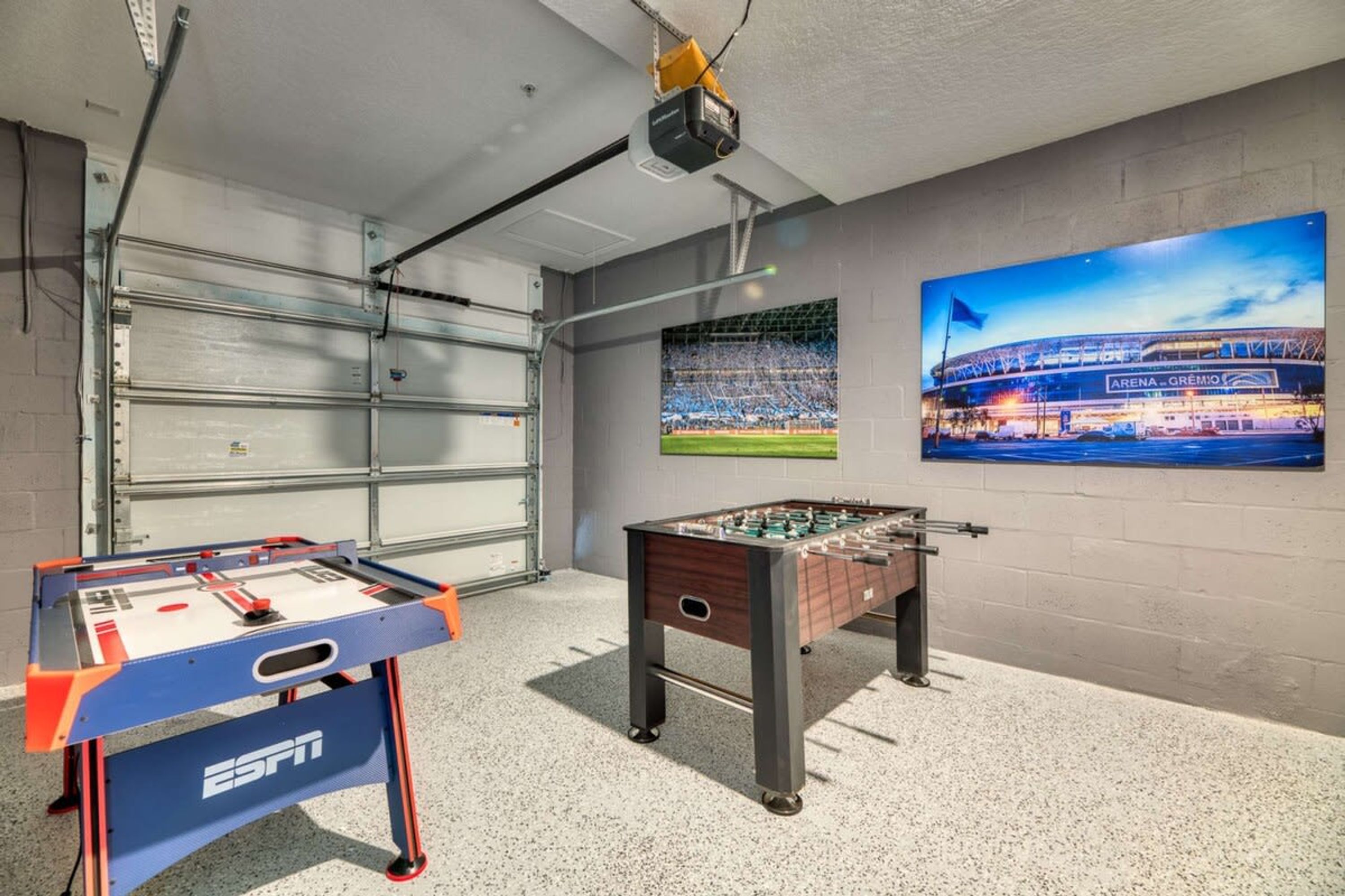 Een kamer met een tafelvoetbaltafel, een beamer en twee posters van een stadion.