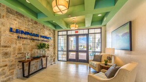 A lobby with a stone wall, a reception desk, a seating area with a sofa and armchairs, and a large glass door leading outside. - Charming 4 BDR Townhome at Storey Lake Resort (Kissimmee)