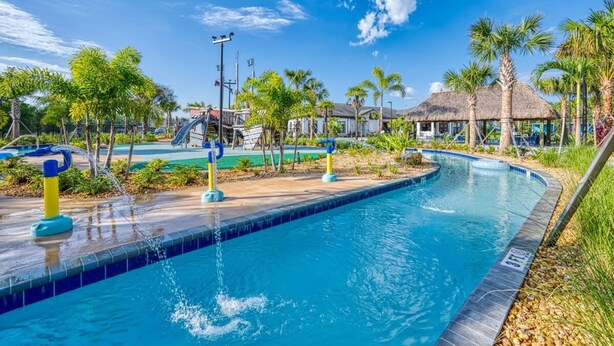 Ein Pool mit Wasserspiel, umgeben von Palmen und einer Struktur mit Reetdach.