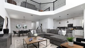 Ein modernes Wohnzimmer mit einem grauen Ecksofa, einem Couchtisch und einem Essbereich mit weißem Tisch und Stühlen.