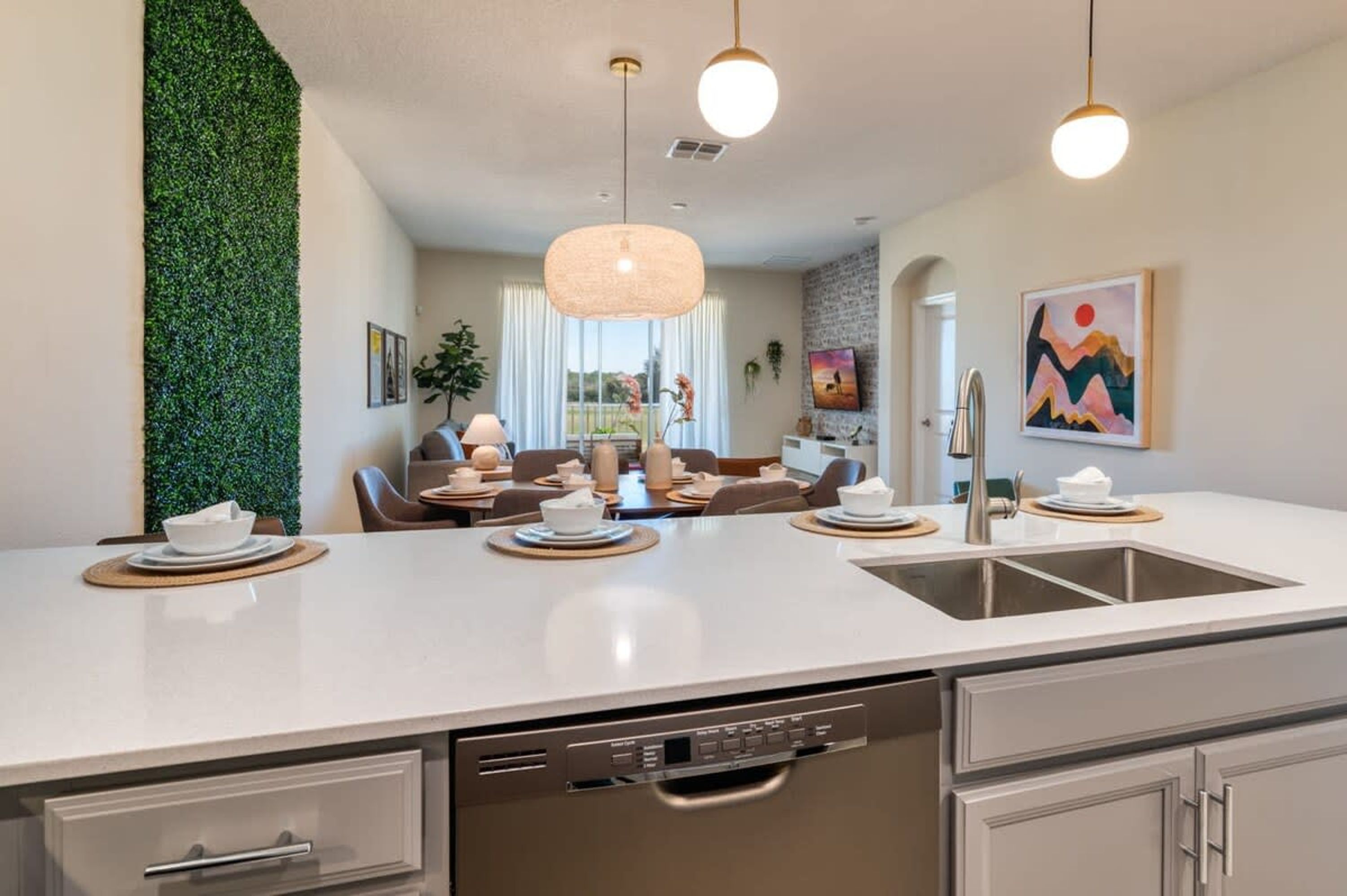 A modern kitchen with a central island, a dishwasher, and a sink. There is a dining area with a table and chairs in the background.