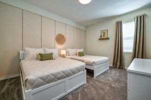 A bedroom with two single beds, a bedside table, a lamp, a small shelf with a decorative item, and a window with curtains.