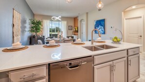 Een moderne keuken met een centraal eiland, een ingebouwde vaatwasser en hangende verlichting.