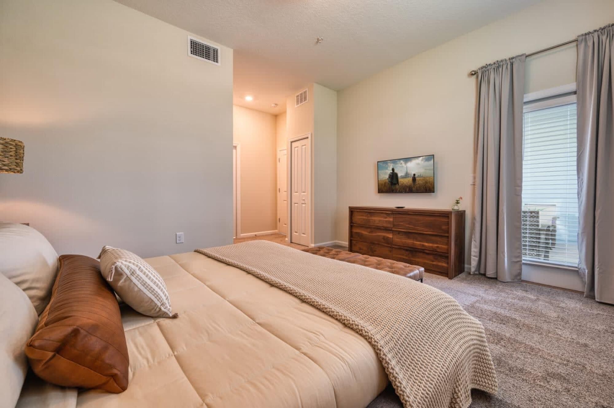 Ein Schlafzimmer mit einem großen Bett, einer Holzkommode, einem Bild an der Wand und einem Fenster mit Vorhängen.