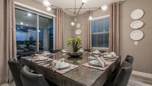 Un coin repas avec une table en verre, six chaises, un vase de fleurs et un lustre moderne.