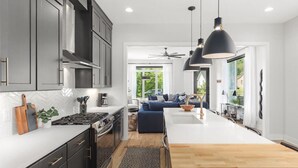 A modern kitchen with dark cabinets, a central island, and a dining area with a blue sofa. - Huge Rooftop Patio at this Stunning Spacious House (Nashville)