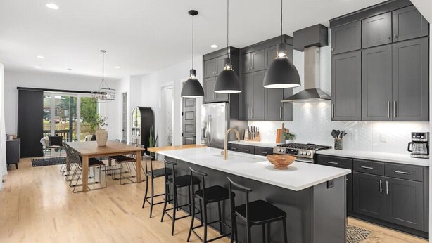 A modern kitchen with dark cabinets, a central island with stools, pendant lighting, and a dining area with a wooden table and chairs. - Huge Rooftop Patio at this Stunning Spacious House (Nashville)